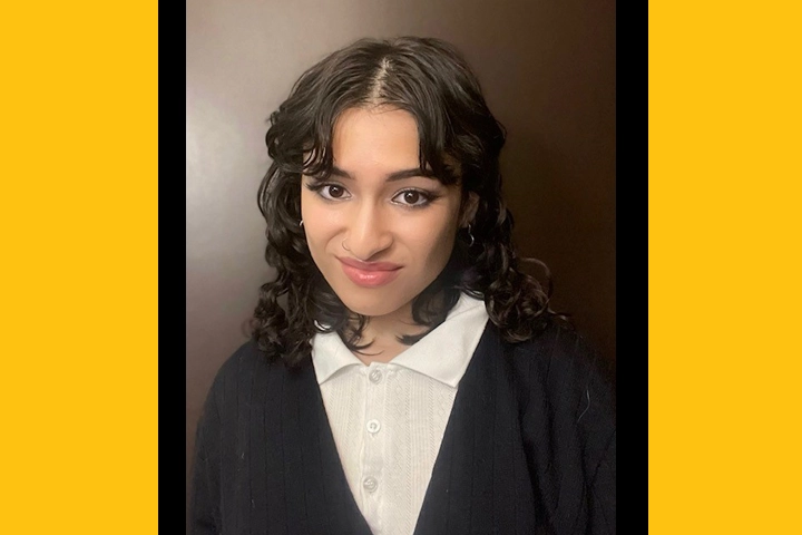 A headshot of a young Latina woman with curly dark hair, wearing a collared shirt and black cardigan.