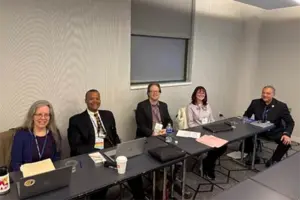Five people sit at a black conference table in a gray room.
