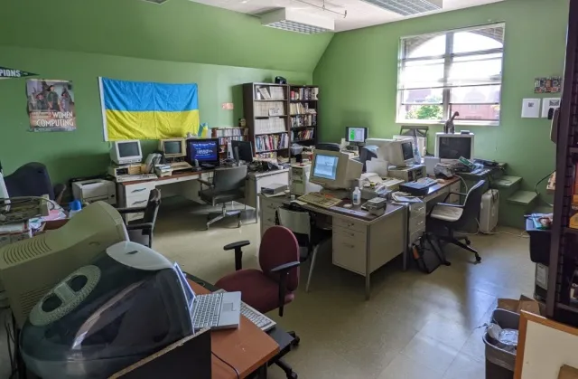 A room of older computers seated on desks around the walls of the room. A Ukrainian flag hands on the green wall.