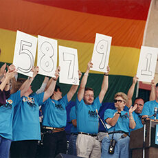 Group of people holding up numbers in front of a Pride flag