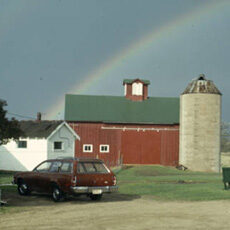 Image of barn, silo, hatchback car with rainbow