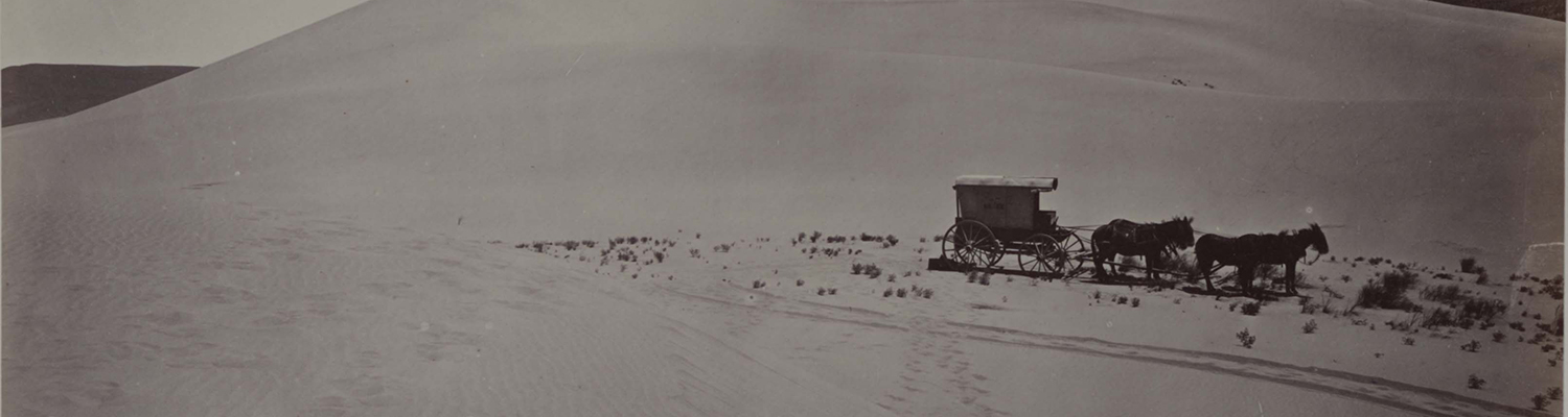 Historic photograph of four horses leading covered wagon across barren landscape