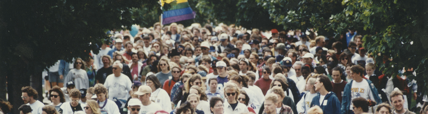 Scene of a crowd walking with a Pride flag in the background