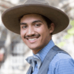 A mans wears blue clothing and a brown hat.