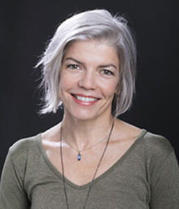 A female professor in a green shirt smiles for a photo.
