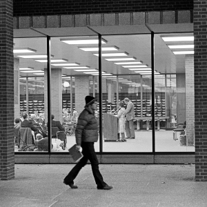 A man walks outside the Golda Meir Library, where an event is taking place indoors.