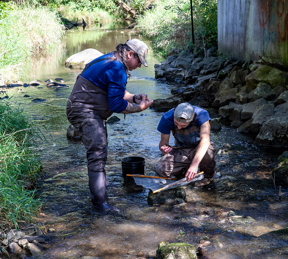 Two students collecting water samples in a creek