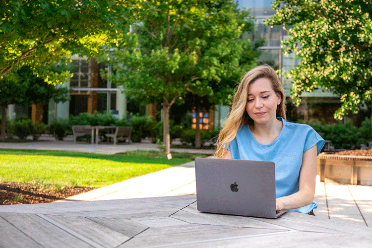 Computer science master's student Catelyn works on her laptop outside. 
