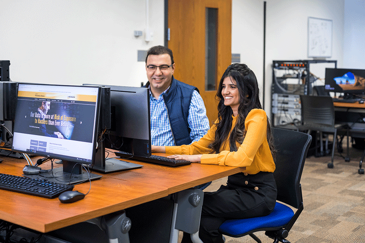 Information science and technology student smiling while working with a faculty member on a desktop computer.