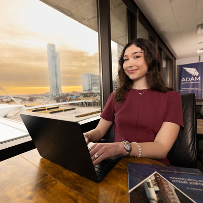 IST major Sisi works on her laptop in front of a window showing the Milwaukee Art Museum