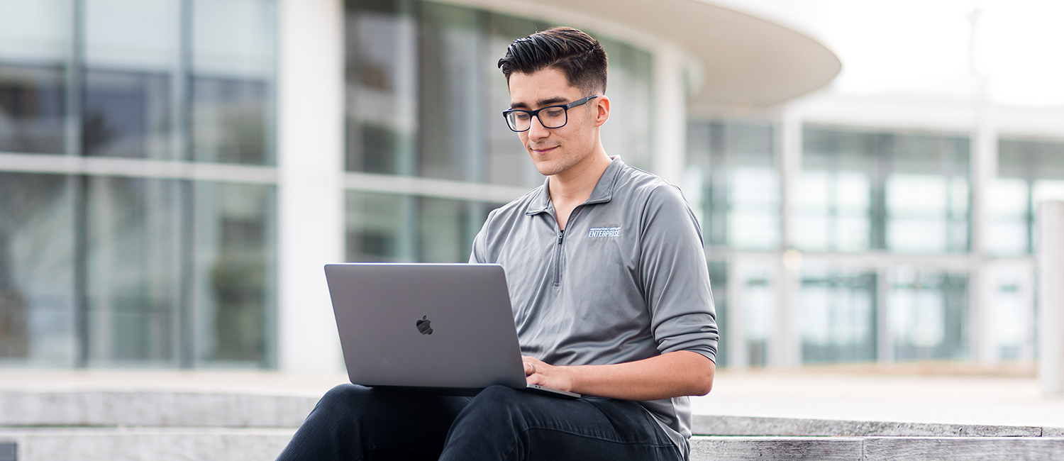 Information technology major Austin Guzman works outside on his laptop in front of Milwaukee's Discovery World