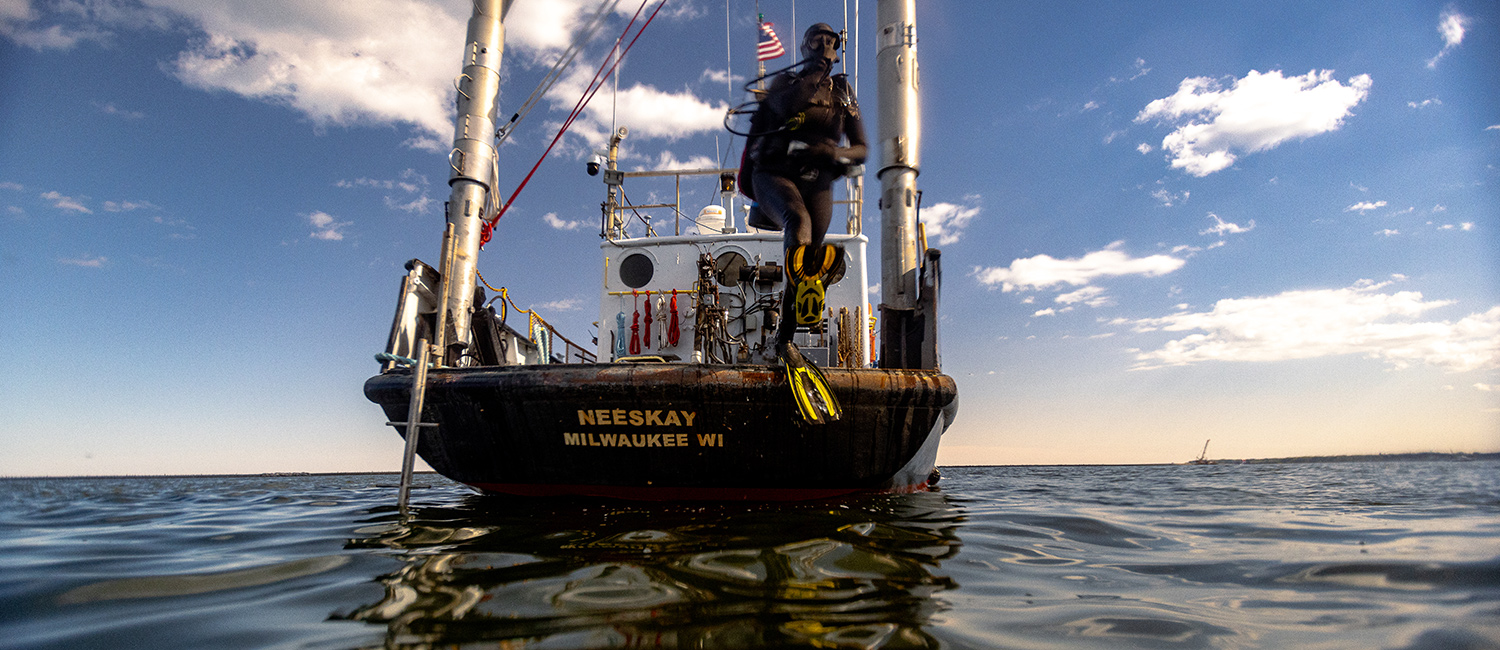 A student wearing scuba gear jumping off the back of the Neeskay into the water.