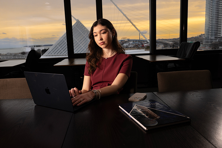 Sidonie, an Information Science & Technology student working on a laptop at her internship with the Milwaukee Art Museum and Lake Michigan in the background.