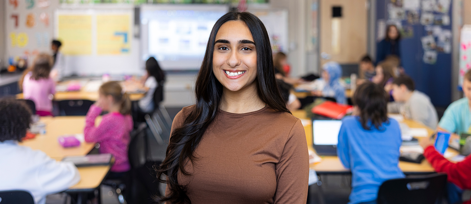 UWM student, Sara, smiling with a classroom of students in the background.