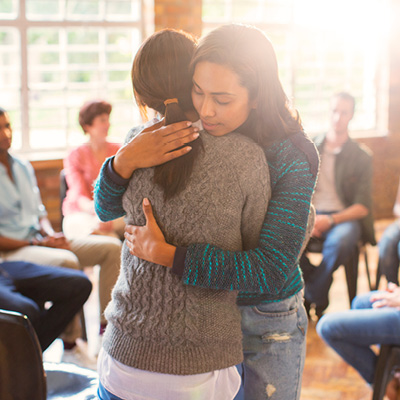 Two women hugging with others in their support group in the background.