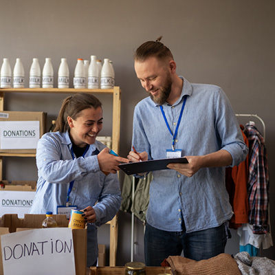 Two people interacting with each other while looking at a tablet surrounded by boxes and items labeled "donation"