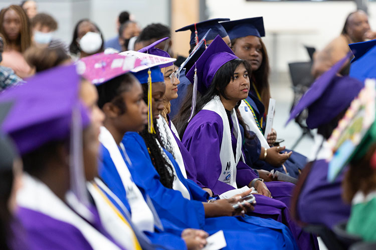 Students in caps and gowns listen to a graduation ceremony speech.