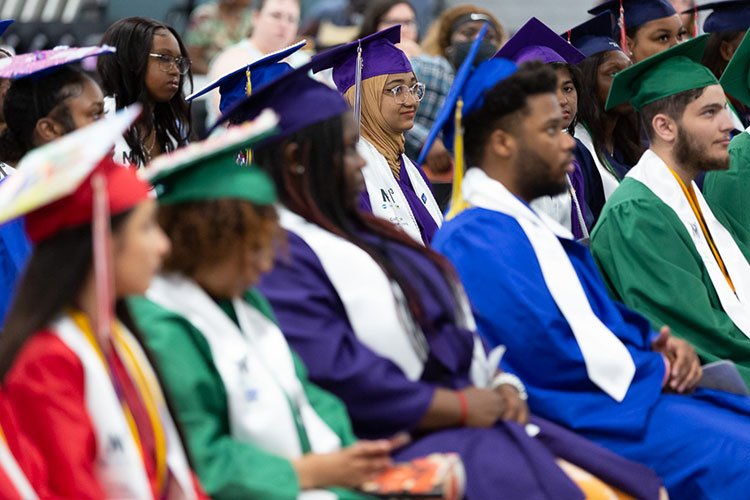 Graduates in caps and gowns listen to a speaker
