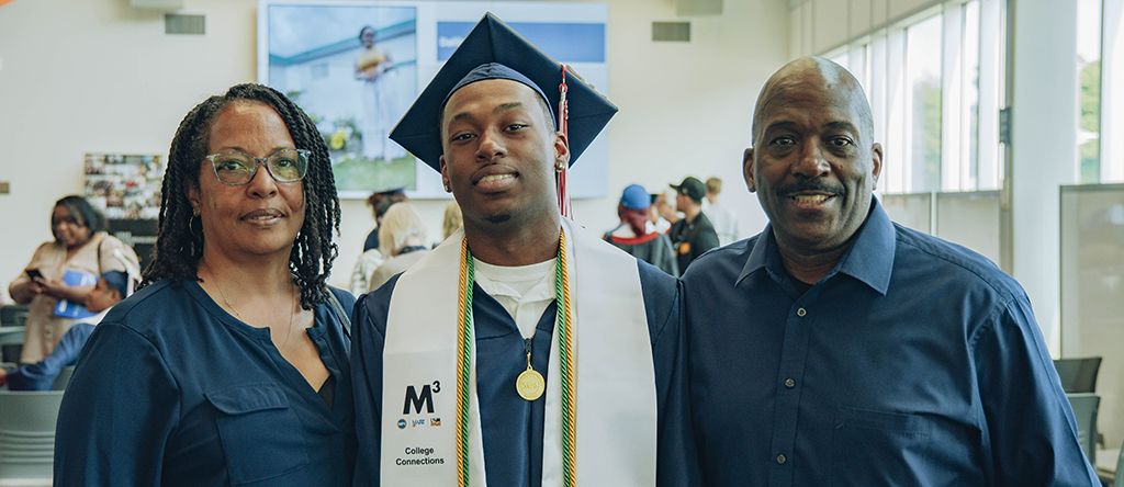 A College Connections student in graduation robes with his parents.