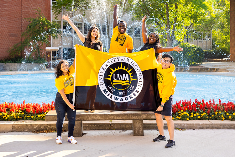 Students holding a UW-Milwaukee flag in front of the fountain on campus