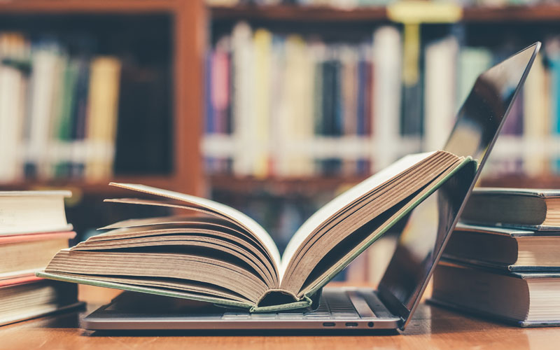 A book open on a table with shelves of books in the background.