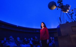 Jean Creighton stands in the planetarium with a blue background.