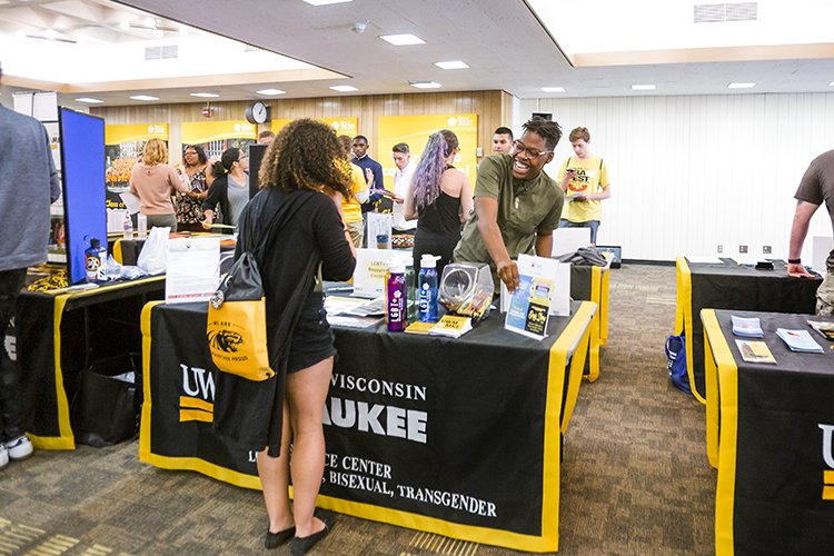 A new student stands at a display table talking with a presenter.