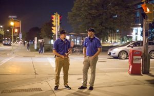 Two students stand on a street corner at night.