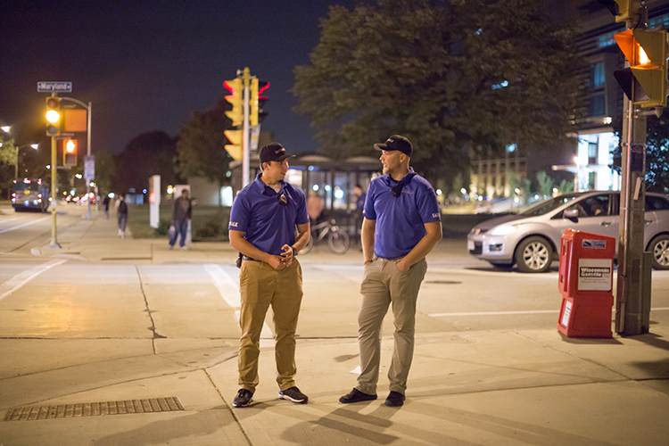 Two students stand on a street corner at night.