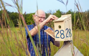 Pete Dunn looks into a birdhouse on a pole in a field.