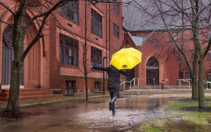 A student runs through the rain with a UWM umbrella.