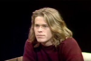 A young Willem Dafoe looks to the side.
