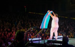 Travis Hard holding up a transgender pride flag for the audience.