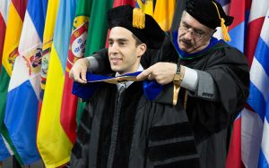 Mohsen, wearing regalia, places a hood over a student in his graduation cap and gown