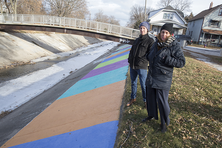 Two people stand along the edge of the concrete channel lining the Kinnickinnic River.