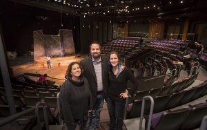 Three people stand in the Mainstage Theatre with the stage in the background.