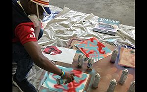 A man crouches as he creates art with spray paint.