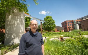 Jim Wasley standing in front of green plants and a tall concrete cistern.