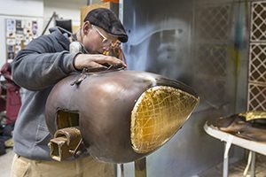 A student works on a metal motorcycle part in a workshop.