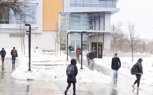 Snow falls as several students walk across the UWM campus.