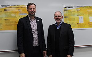 Two men stand in front of a whiteboard.