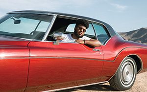 Khalid leans out the window of a red car.