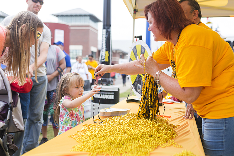 A woman in a yellow shirt hands a gold bead necklace to a small girl.