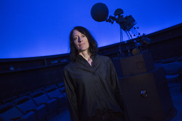 Dawn Erb stands in the planetarium with the projector in the background.