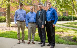 Four men stand in a row in front of a building.