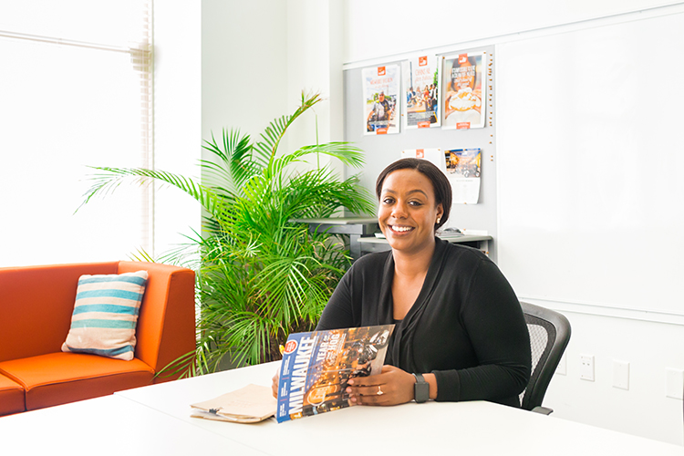 A woman sits at a table while writing notes along side a visit milwaukee magazine.