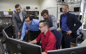 Five men work on a computer.