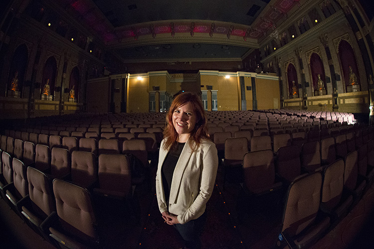 A woman stands amid rows of theater seats.