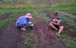 Two students sit on the ground working with plants.
