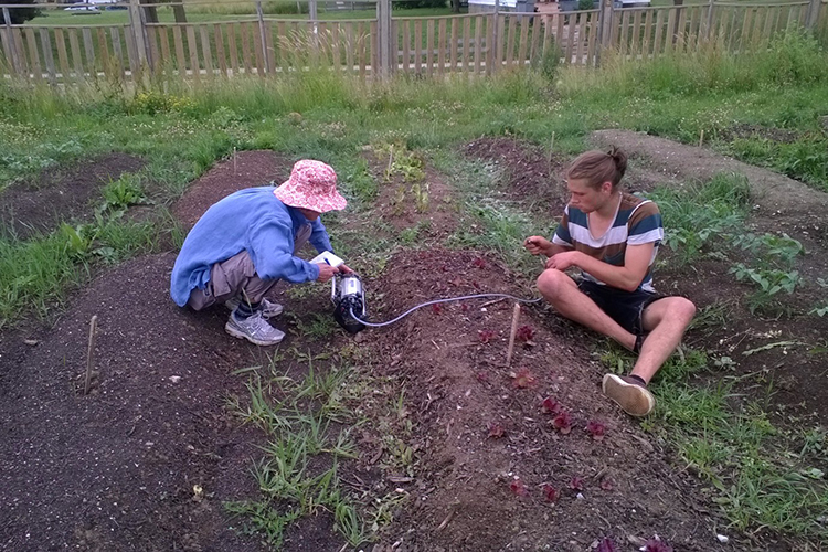Two students sit on the ground working with plants.